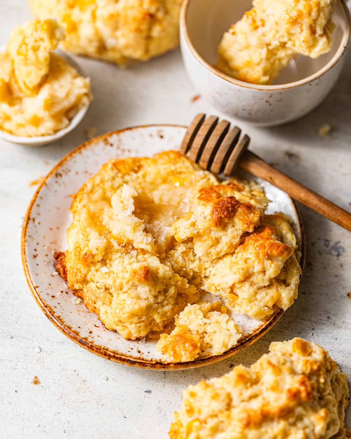 cornbread biscuits on a plate with a honey dipper with a smear of honey butter melted into the biscuits.