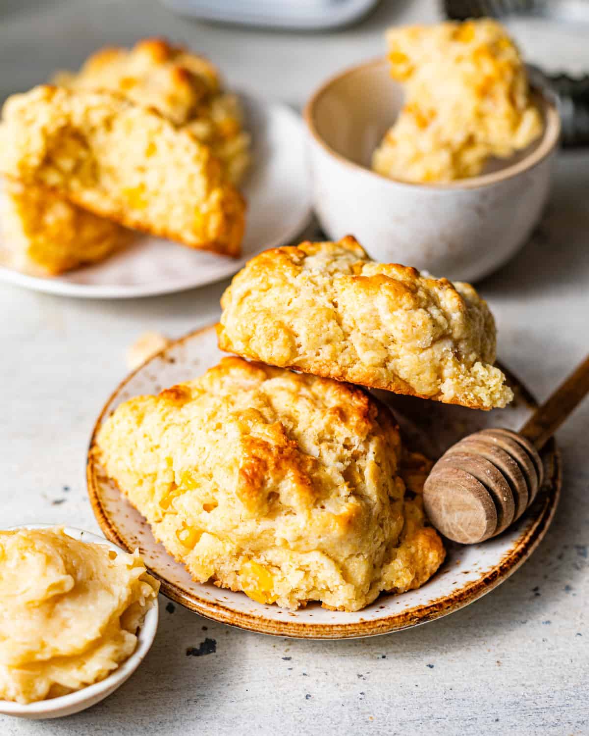cornmeal biscuits stacked on a ceramic plate beside a small bowl of honey butter.