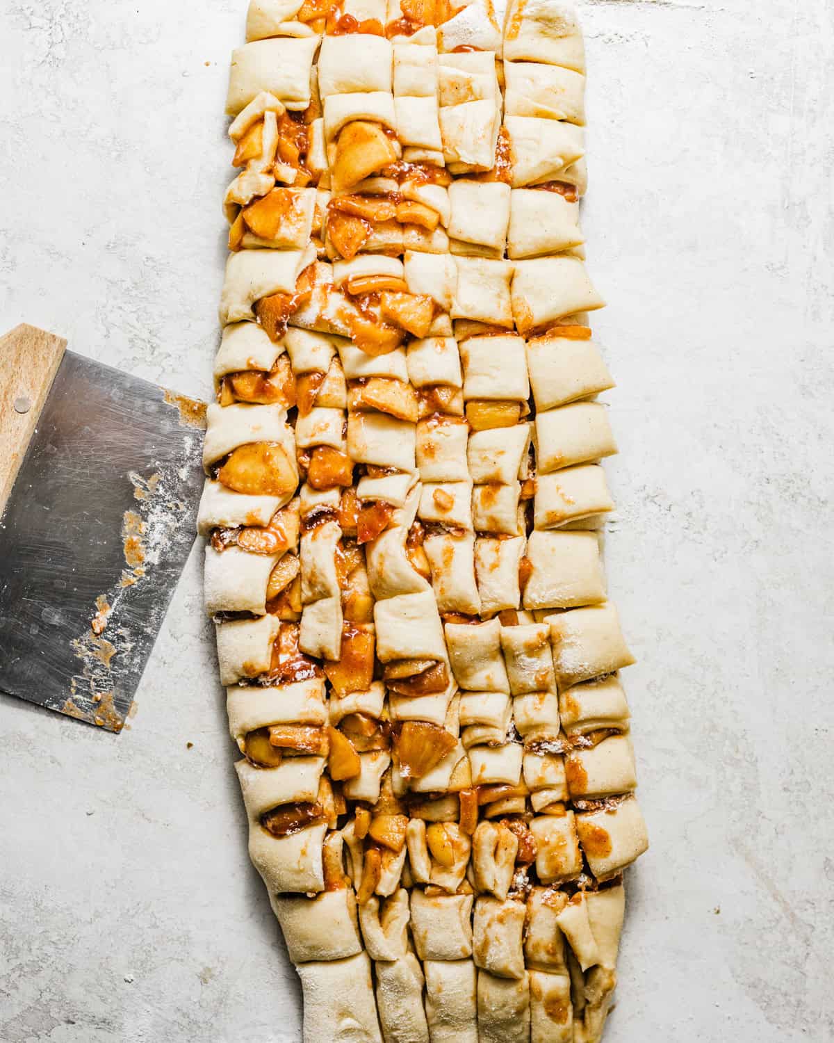 Yeasted apple fritter dough chopped into small pieces with cinnamon-spiced apple filling before shaping into fritters.