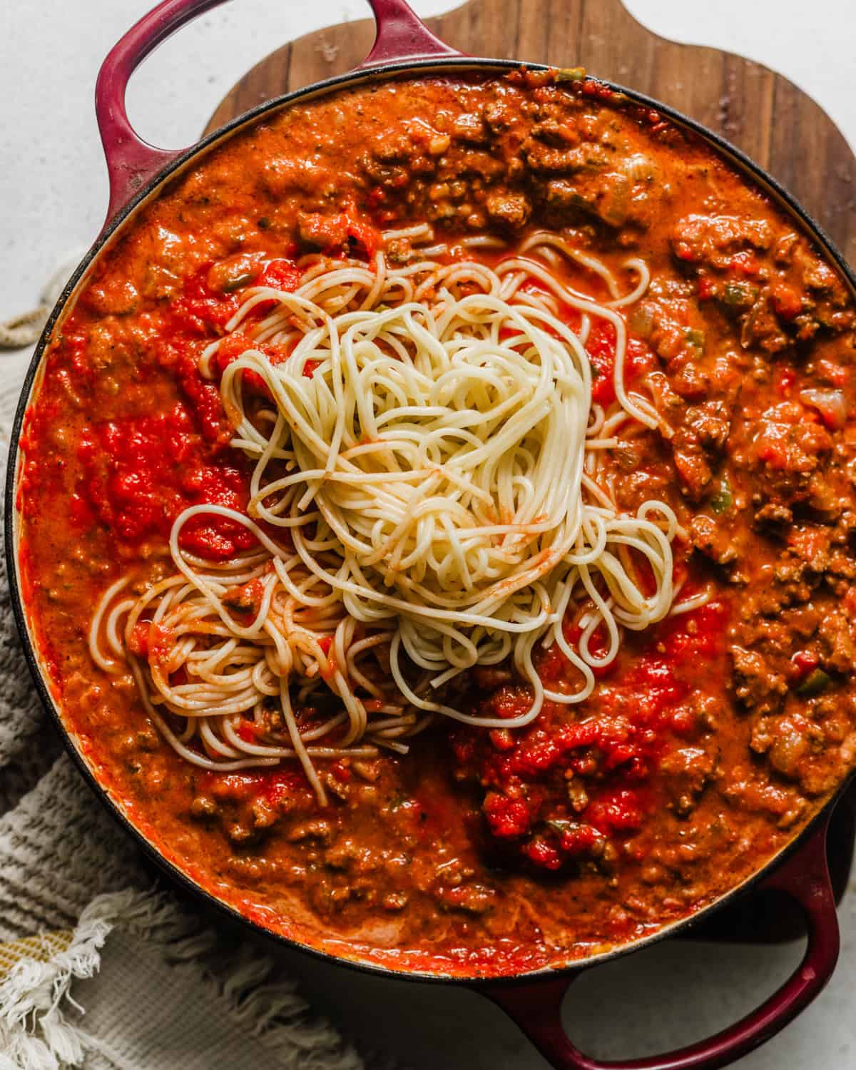 cooked spaghetti being added to the meat sauce. 
