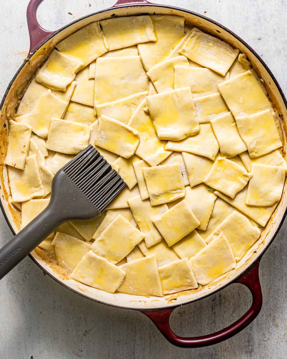 chicken pot pie filling in a pan topped with sheet of puff pastry that's been brushed with egg wash before baking.