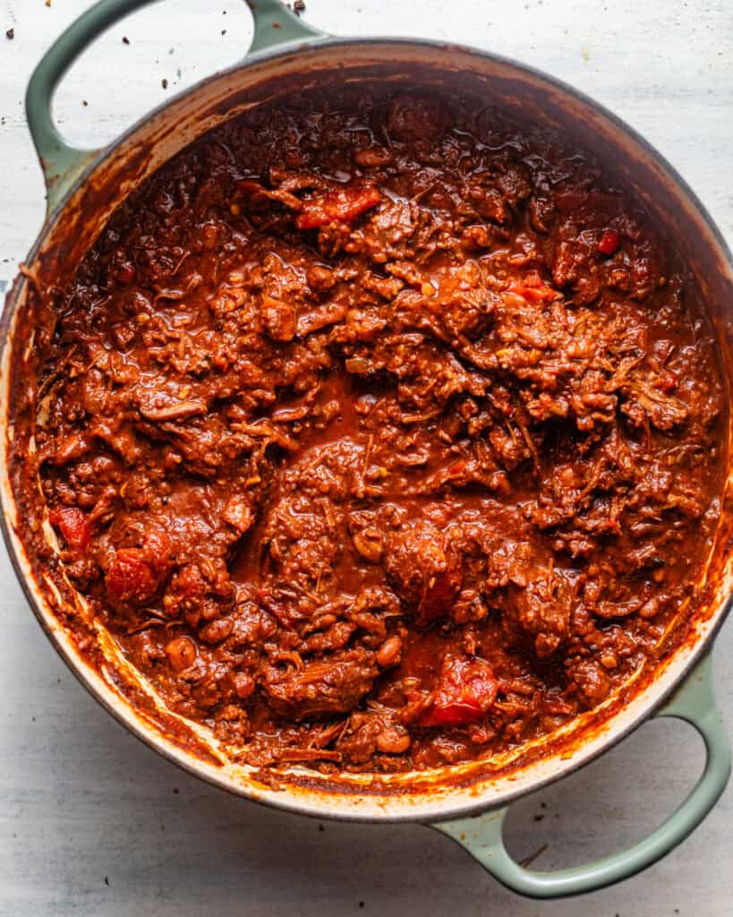 Thick, hearty chuck roast chili with tender shredded beef, ground beef, and beans in a rich, smoky tomato sauce inside a Dutch oven.