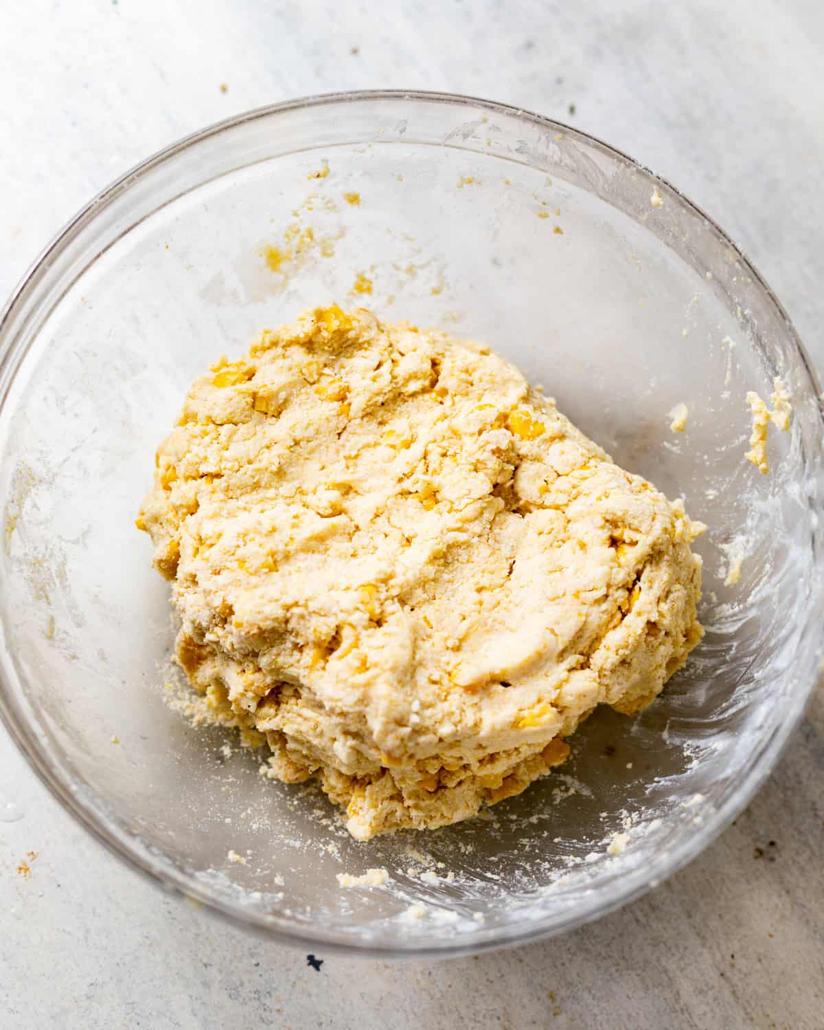 Homemade cornbread biscuit dough with visible sweet corn kernels mixed together in a large glass bowl.