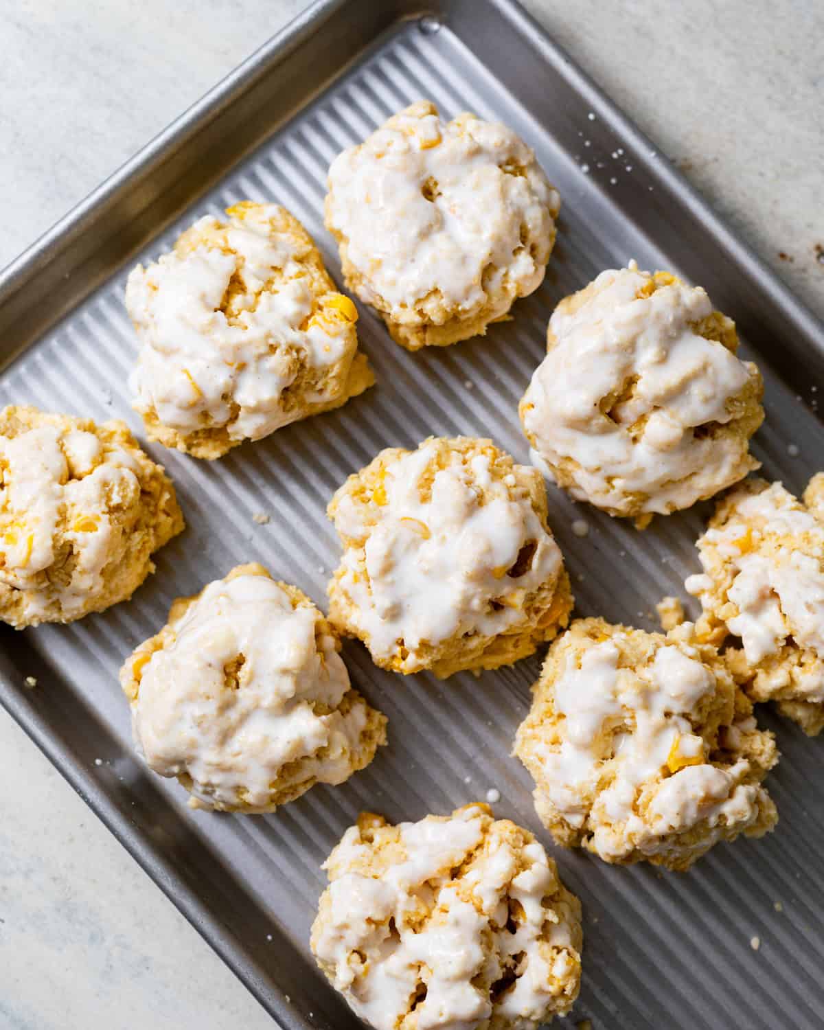 Unbaked cornbread biscuits scooped into rustic mounds and brushed with buttermilk on a metal baking sheet.