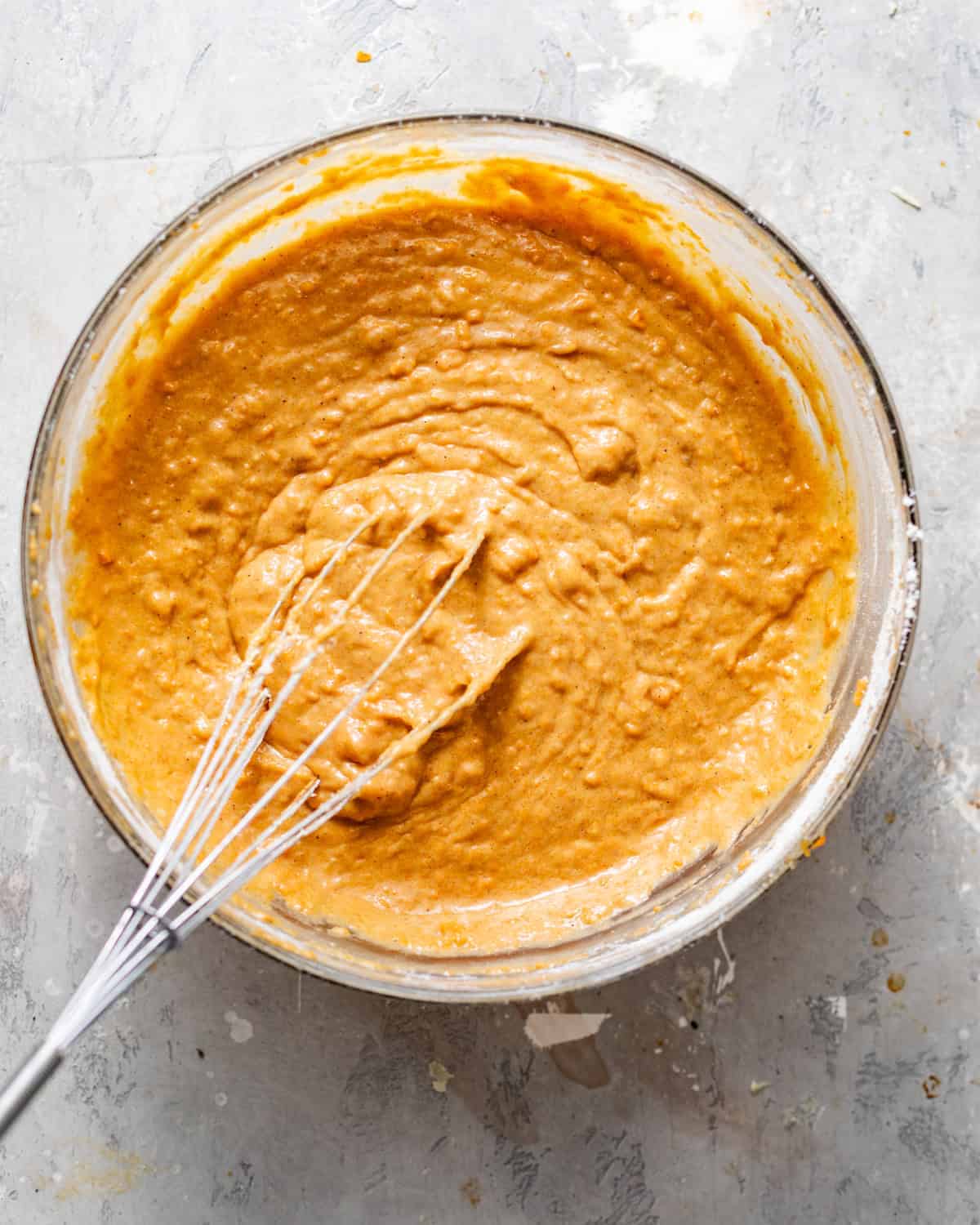 Smooth, cinnamon-spiced cake batter in a glass mixing bowl with a whisk, ready to pour into cake pans.