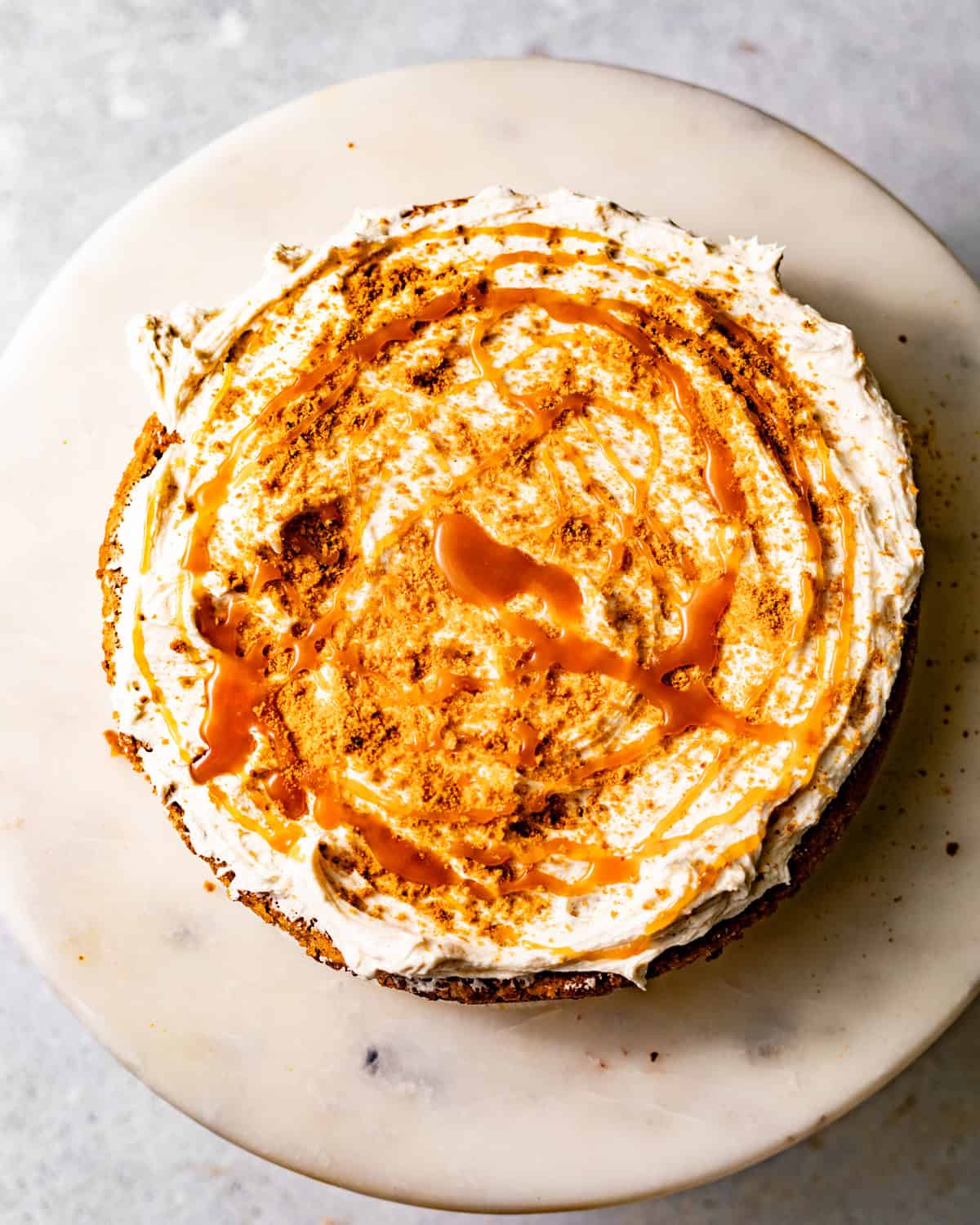 spice cake being assembled with brown butter cream cheese frosting, crushed gingersnaps, and buttermilk syrup drizzled on top.