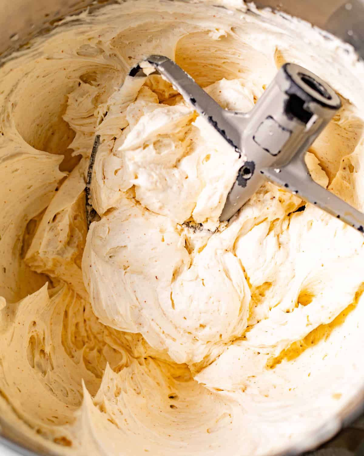 Fluffy brown butter cream cheese frosting in a stand mixer bowl with the paddle attachment.
