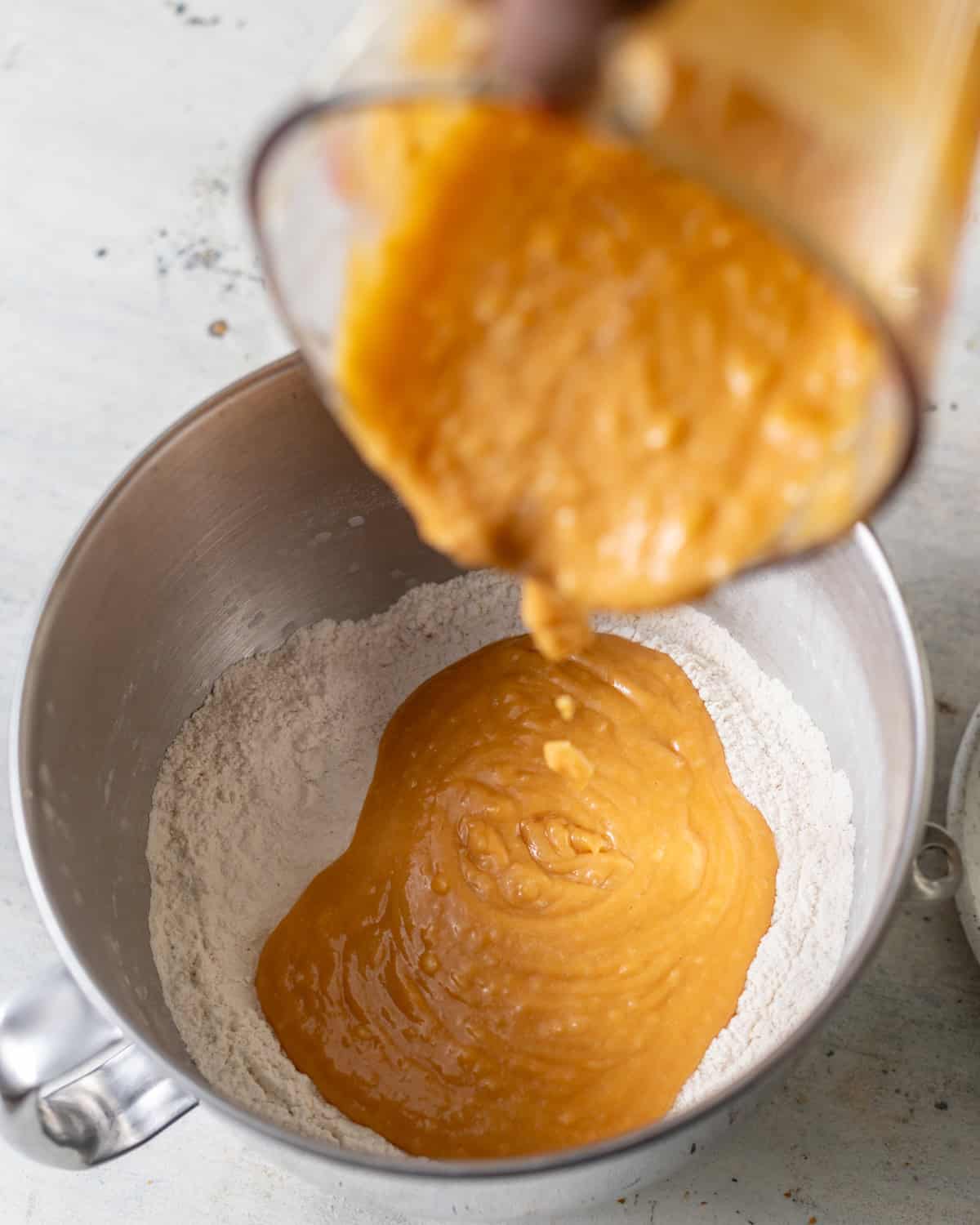 sweet potato mixture being poured into the dry ingredients before kneading to form the cinnamon roll dough.