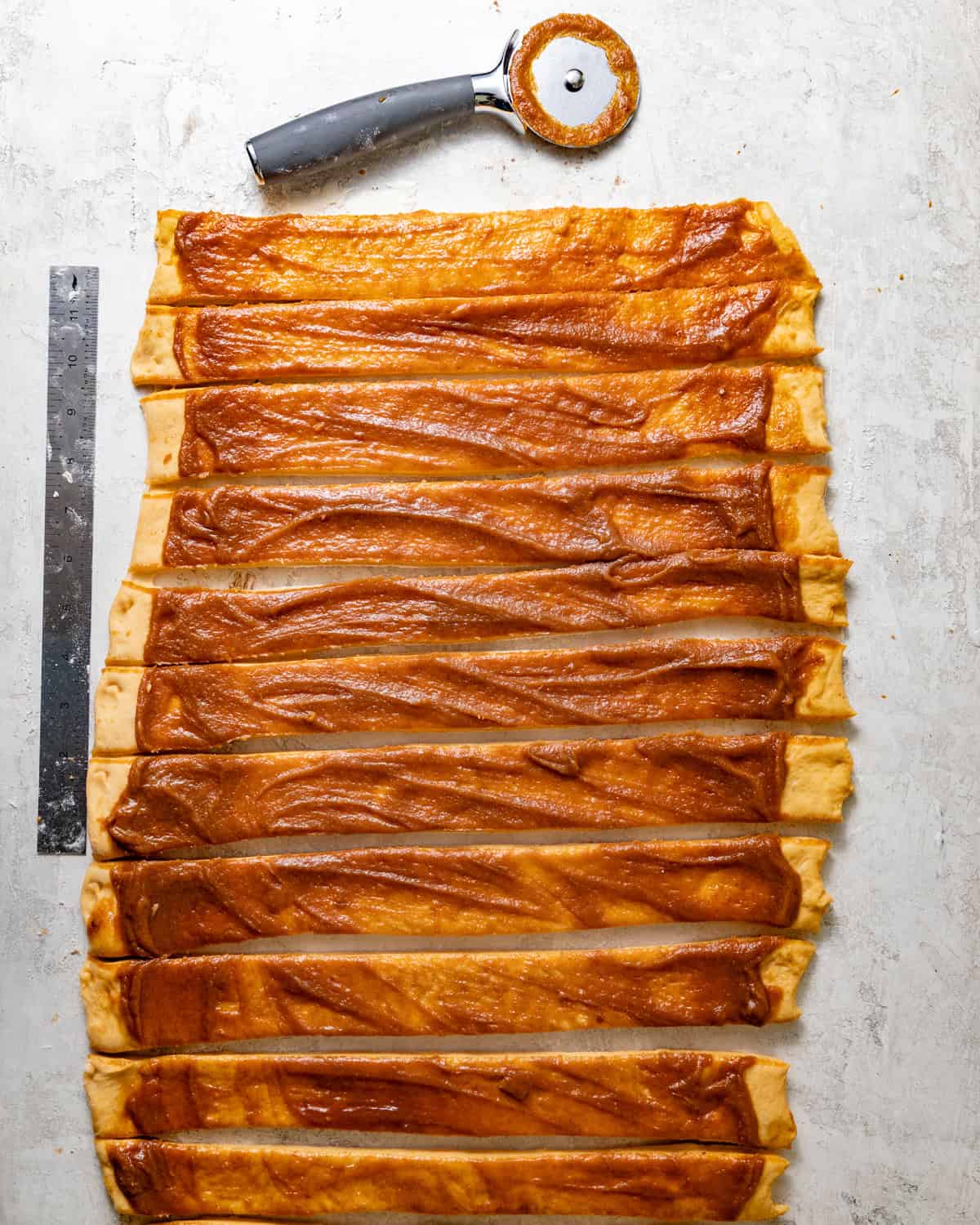 cinnamon roll dough rolled out into a rectangle with sweet potato filling spread on top and the dough cut into 12 equally sized strips.