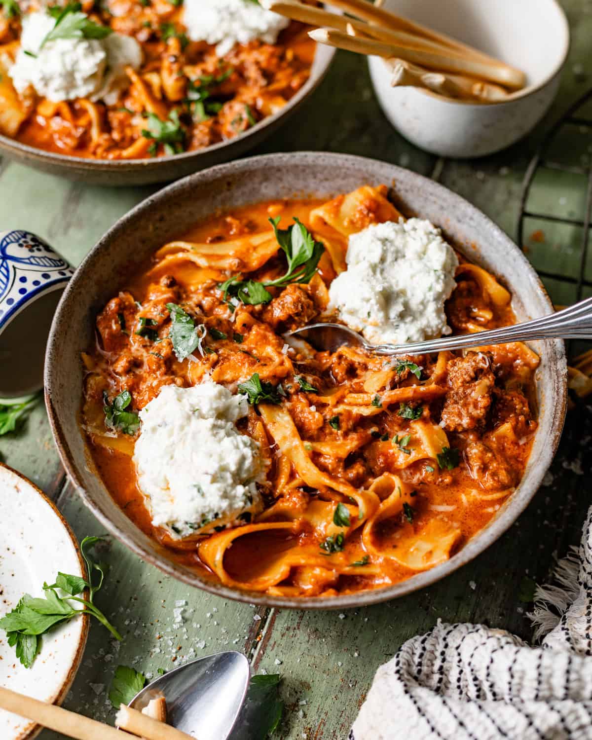slow cooker lasagna soup in a bowl with a spoon topped with ricotta and fresh herbs.