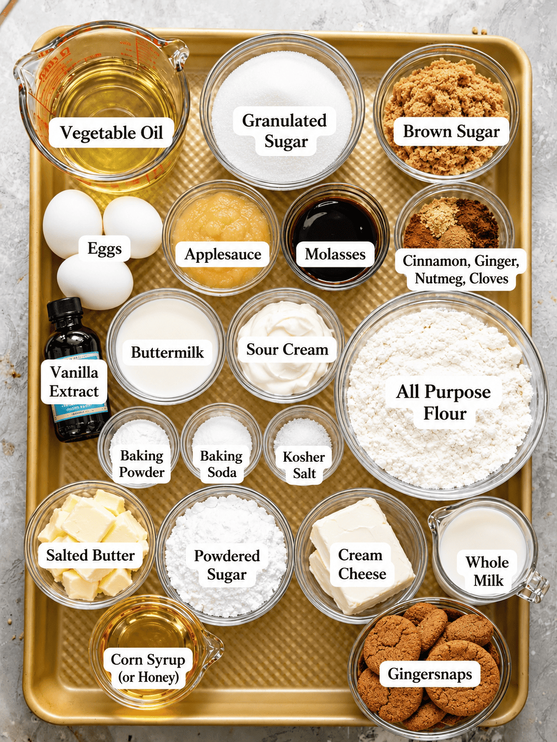 ingredients to make spice cake on a baking tray - flour, baking soda, baking powder, vegetable oil, eggs, brown sugar, sugar, butter, gingersnaps, sour cream, buttermilk, cinnamon, nutmeg, ginger, and cloves.