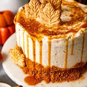 spice cake on a cake stand drizzled with buttermilk syrup and crushed gingersnaps and decorated with maple leaf cookies.