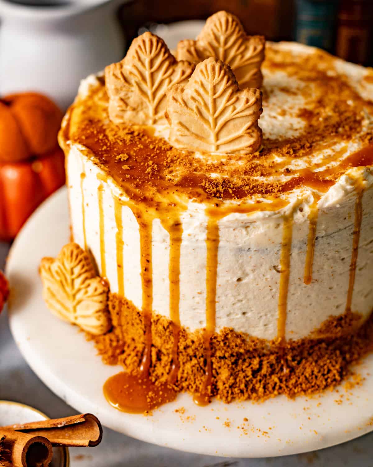 spice cake on a cake stand drizzled with buttermilk syrup and crushed gingersnaps and decorated with maple leaf cookies.