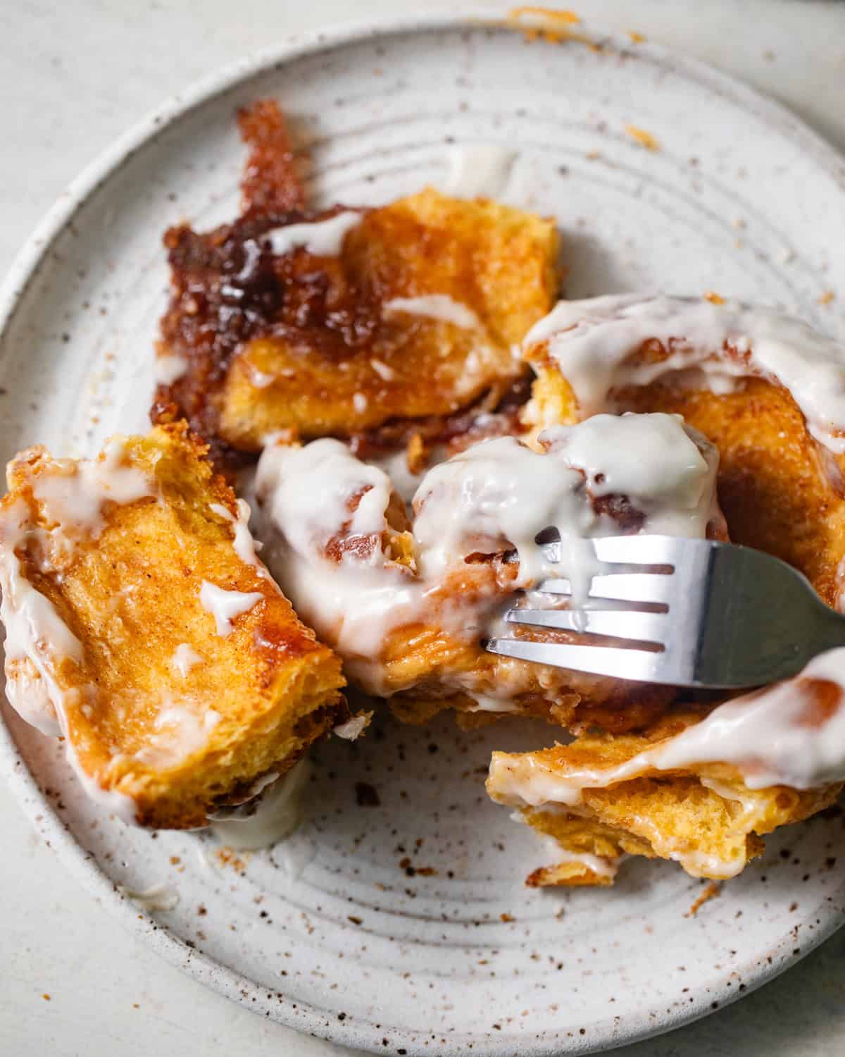 Soft, fluffy sweet potato cinnamon rolls torn into pieces, revealing a tender golden-orange interior, gooey cinnamon sugar filling, and rich cream cheese frosting melting over the rolls on a ceramic plate.