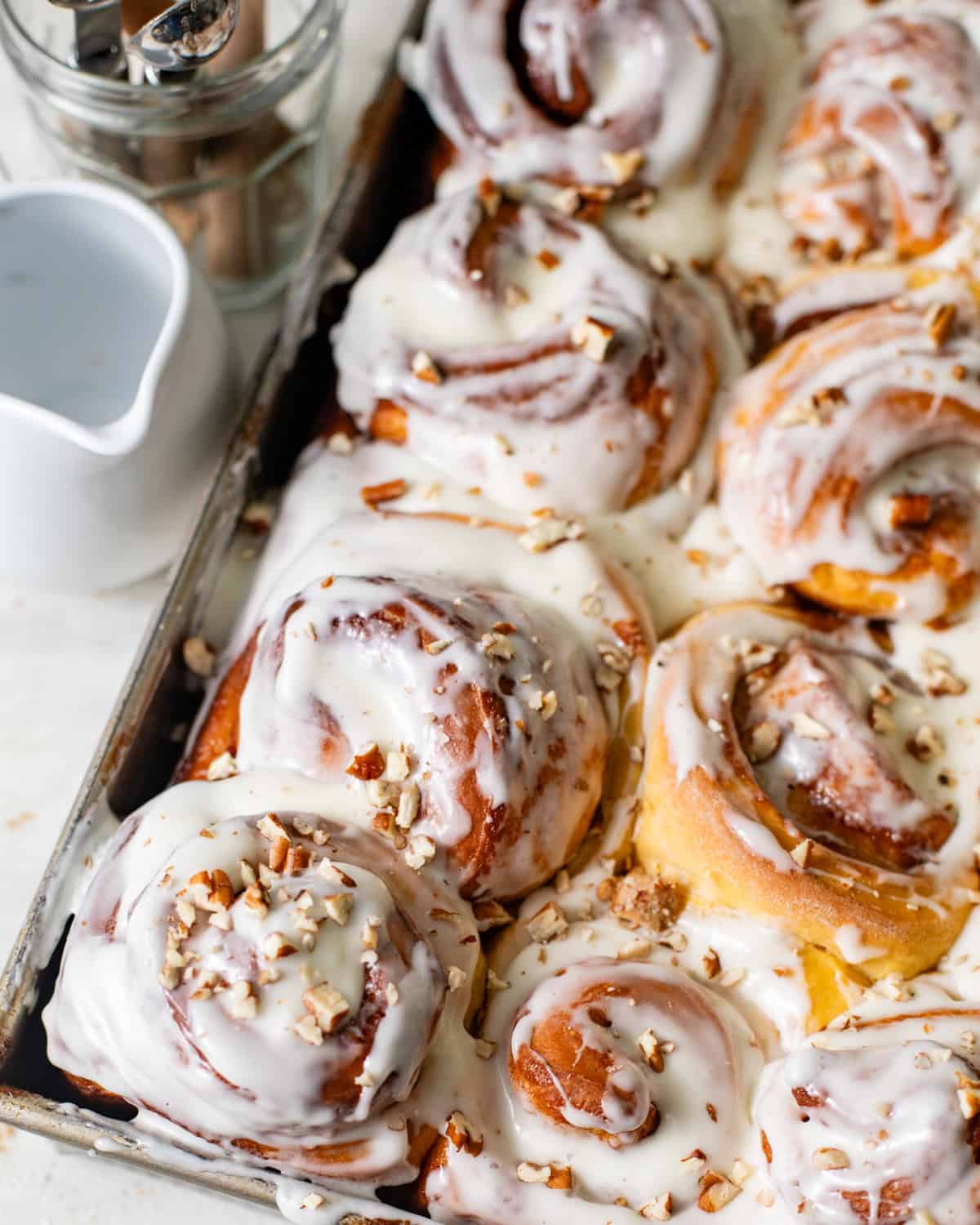 frosted sweet potato cinnamon rolls baked in a pan topped with chopped pecans.